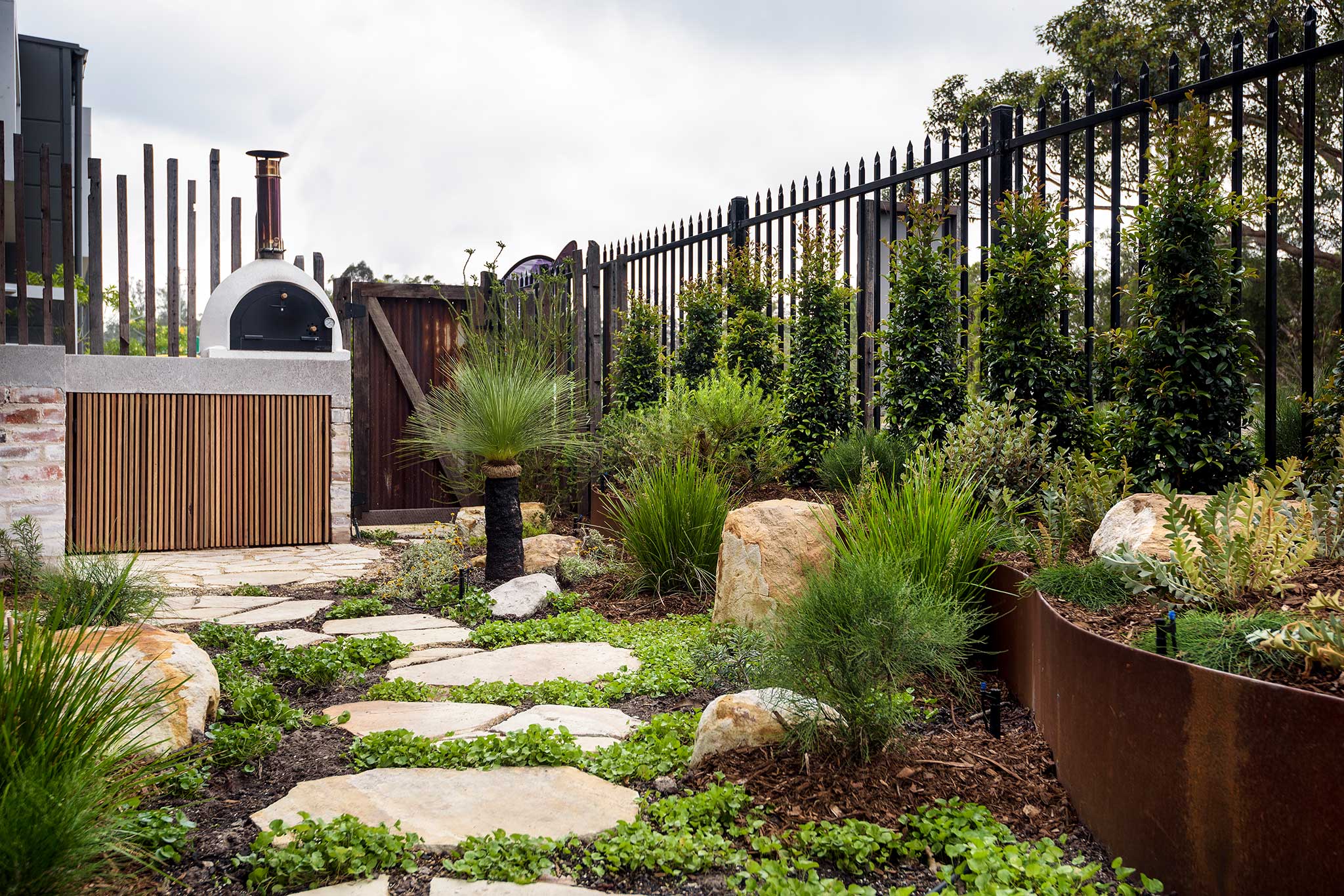 MBS native courtyard landscape design showing paved pathway, groundcover, native plants, wood fired oven and garden beds