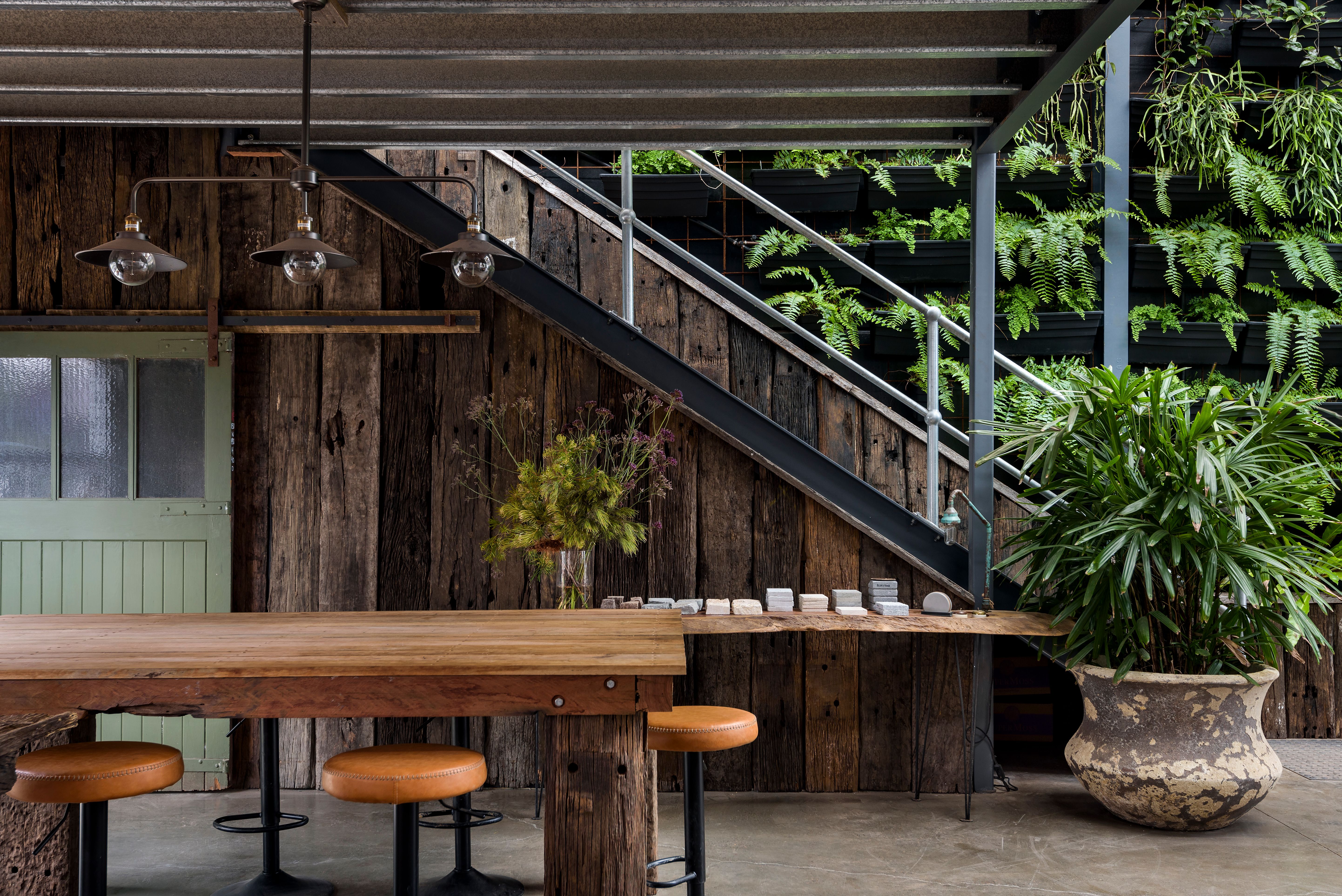 Interior fit-out and styling my Moss Boss Studios, with recycled railway sleeper cladding and green sliding barn door under stairs, custom-made timber tables, feature pot plant, vertical garden and rustic light fitting