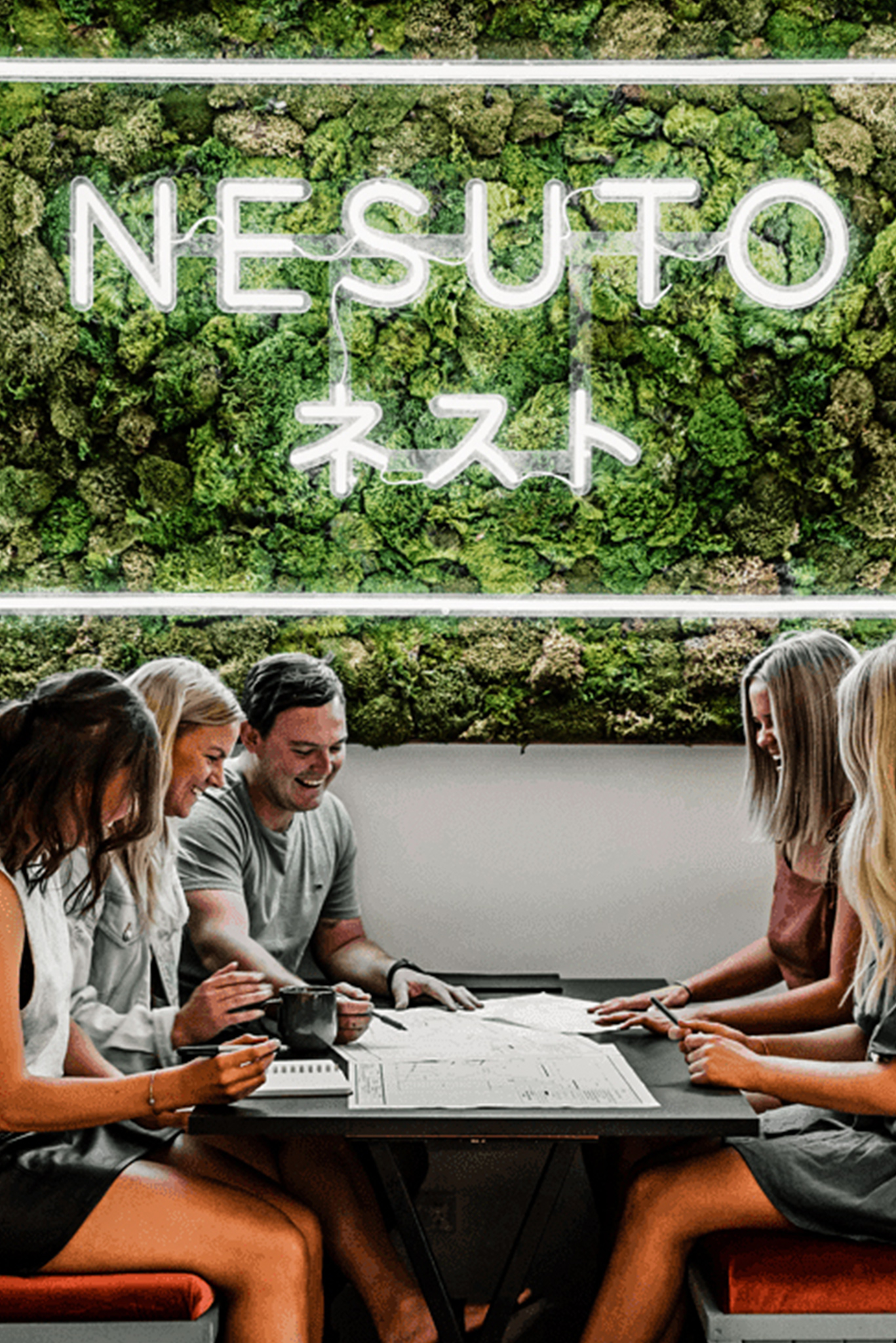 Moss installation with neon sign reading 'Nesuto' above coworking table